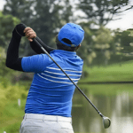 A man in a blue shirt and white pants is engaged in a golf game, focusing on his swing.