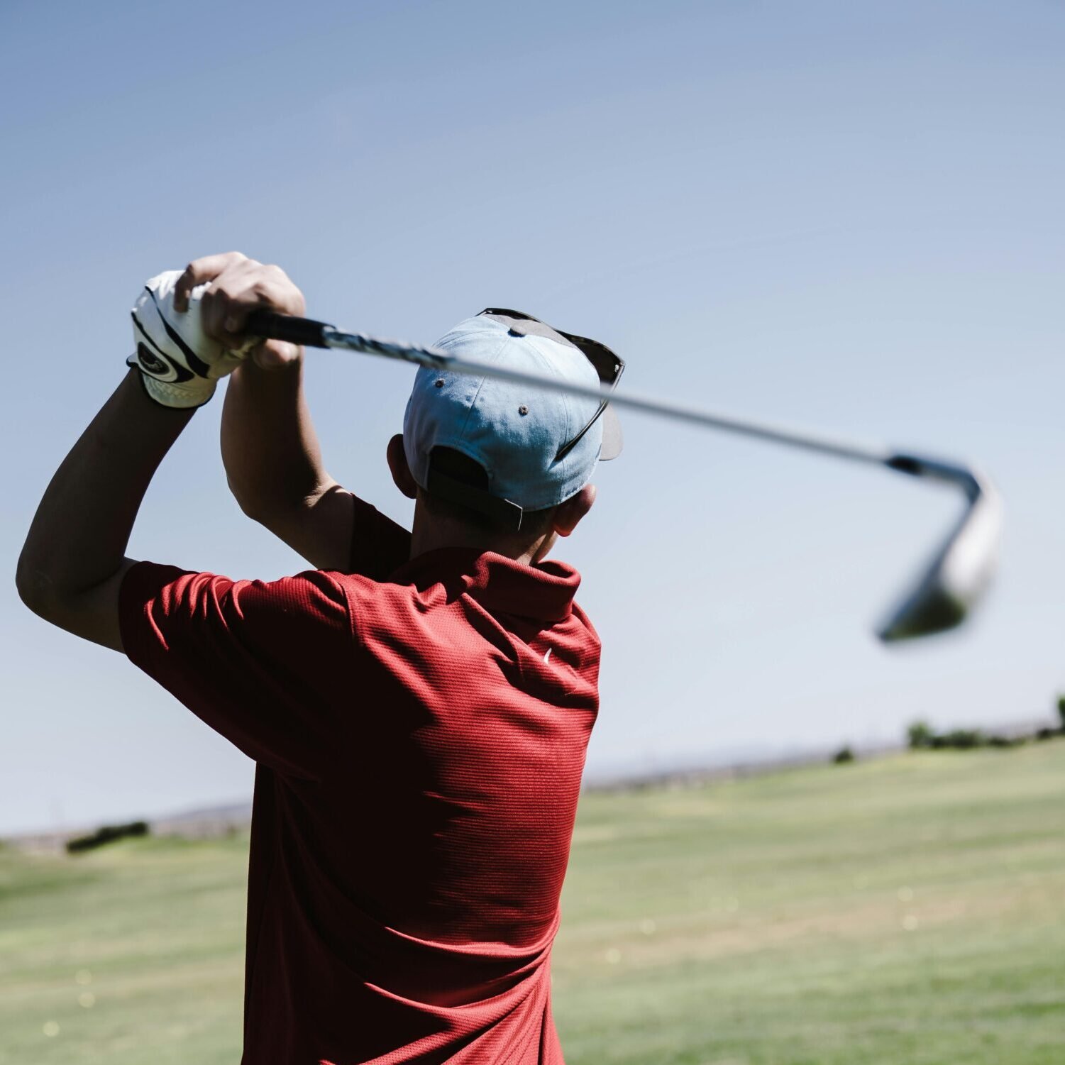 Man Swinging Golf Club Facing Grass Field