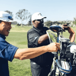 Two men holding golf clubs, one putting clubs into a Callaway Capital golf stand bag.