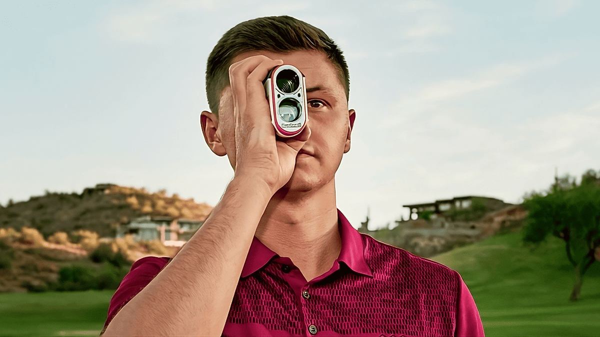 A man holds a golf club in front of his face, showcasing precision and focus, with a top-rated rangefinder nearby