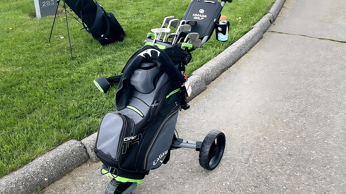 A Trilite golf push cart and a golf bag are positioned on the roadside, highlighting a moment of leisure in golf.