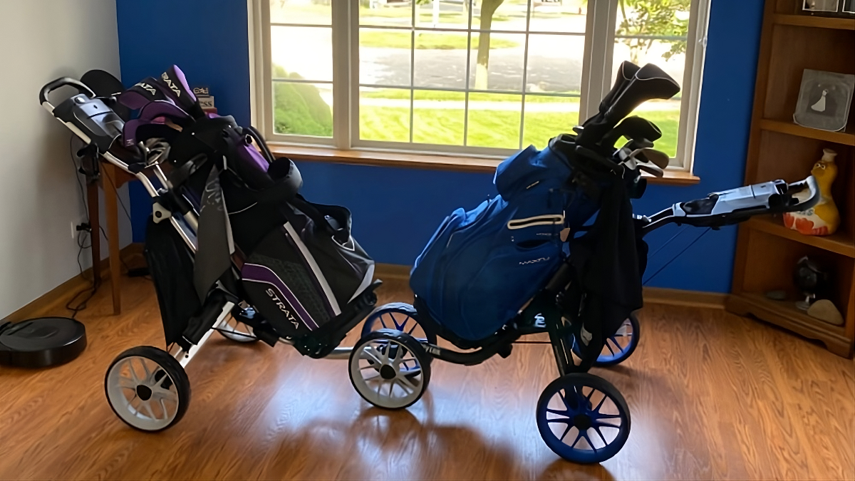 Two golf bags on a Caddytek Caddylite EZ V8 push cart, with a window visible in the background.